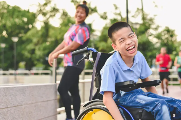 A carer smiling as a child is happily using a new wheelchair that the physiotherapist from LiveWise Health provided.